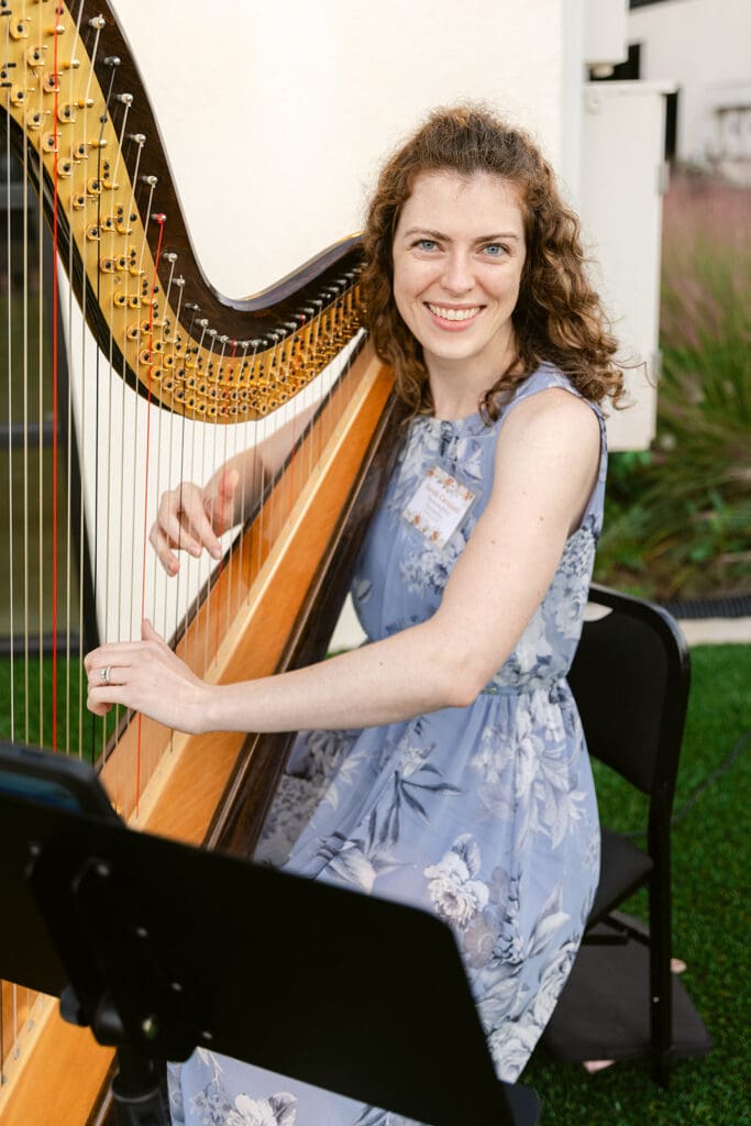 Harpist in blue dress smiles directly at the camera while playing