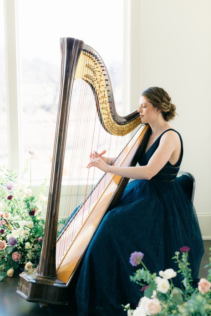 Harpist in ballgown plays surrounded by purple and white floral arrangements