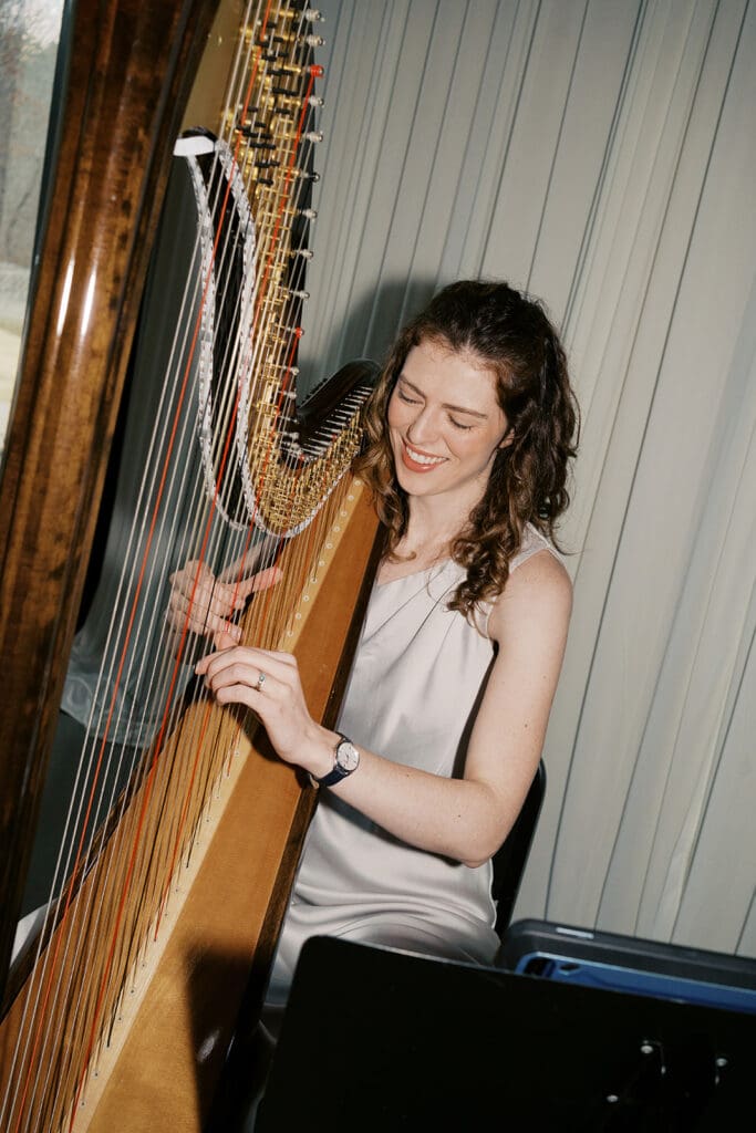 Wedding musician playing the harp smiles while looking down from the camera