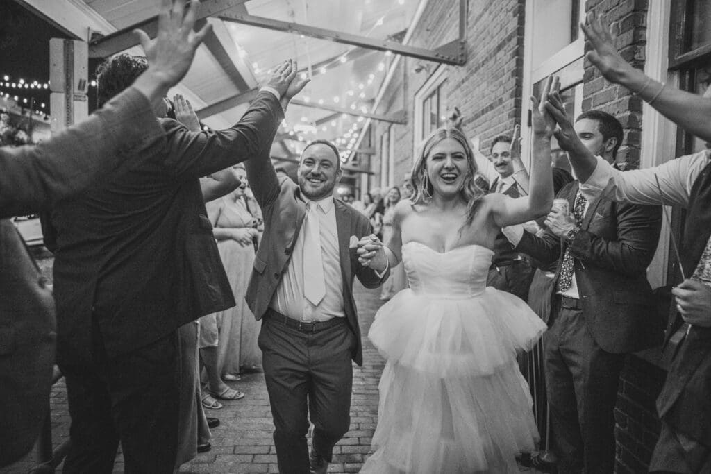 Bride and groom walk through a tunnel of their wedding party, giving everyone high-fives